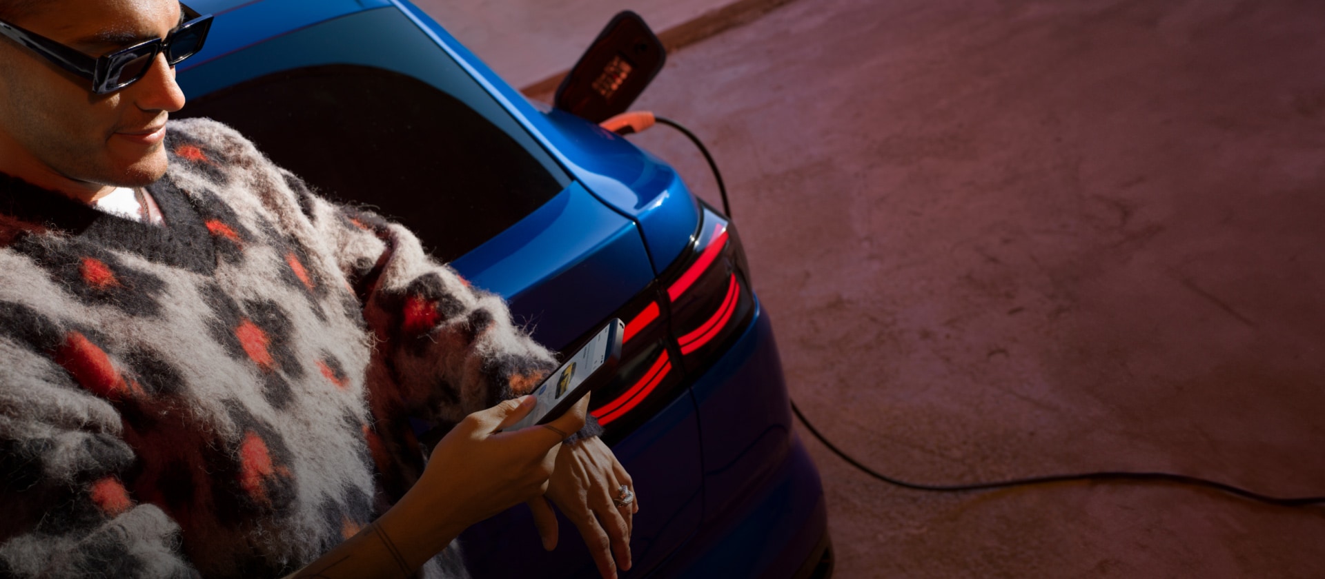 O persoană care încarcă un Ford Capri EV albastru la o stație publică de încărcare.
