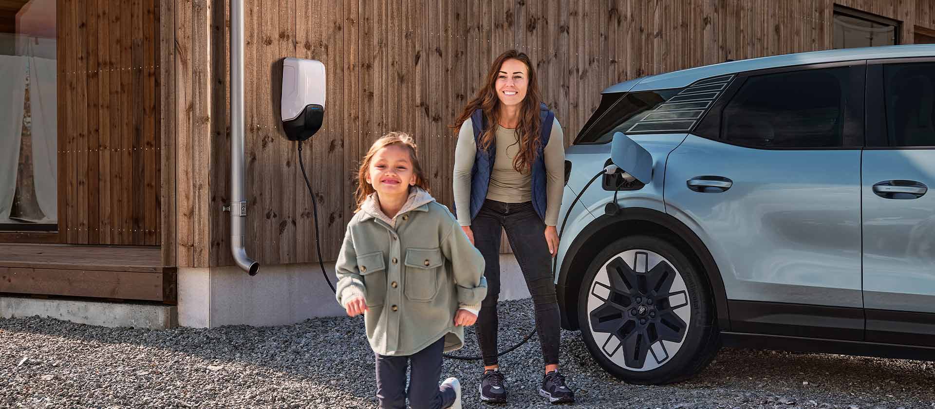 O familie care se distrează în timp ce își încarcă Ford Explorer electric cu un încărcător de acasă pentru vehicule electrice în aer liber.