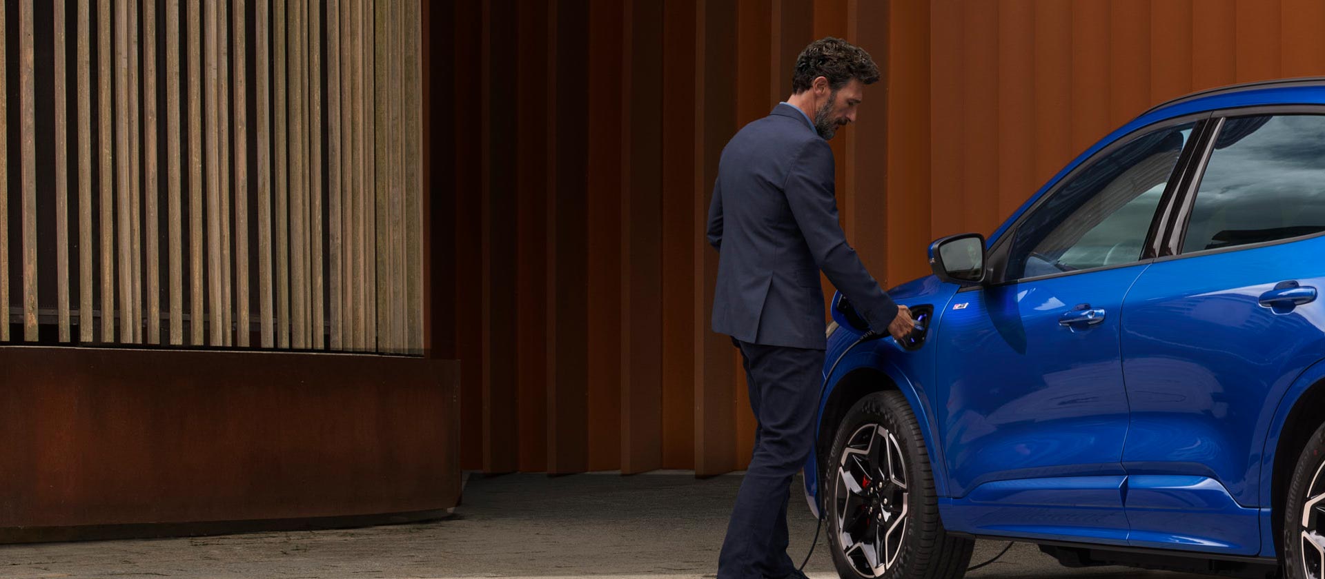 O persoană care conectează o mașină hibrid plug-in Ford la un cablu de încărcare pentru casă EV.