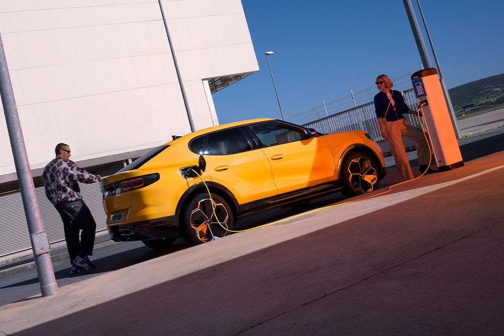 Oameni care încarcă un Ford Capri EV galben la o stație publică de încărcare.