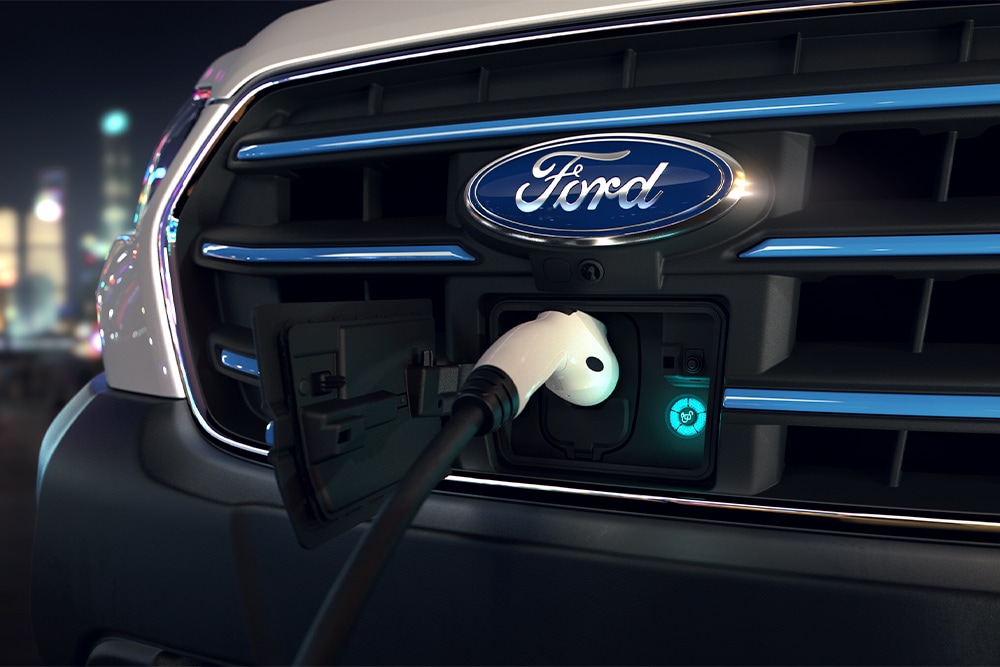 Prim-plan al unui punct de încărcare a unei furgonete Ford E-Transit și al ecusonului Ford oval albastru pe grila din față.