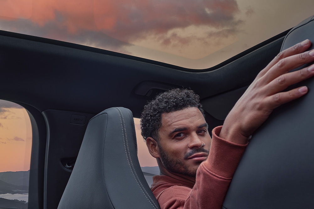 Un bărbat stând într-o mașină la apus, cu mâna sprijinită pe spătarul unuia dintre scaune.