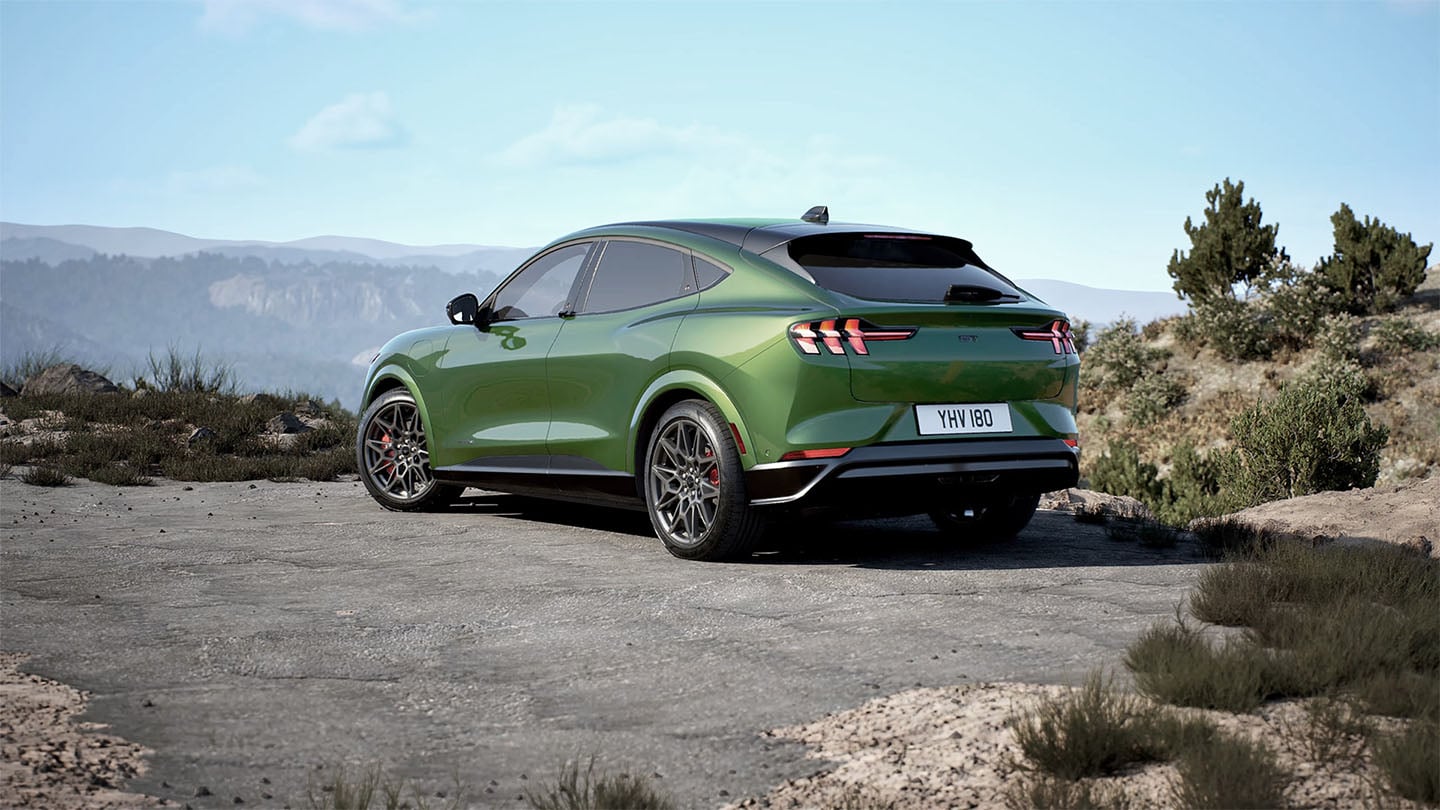 Spatele modelului Ford Mustang Mach-E GT în culoarea Eruption Green parcat pe un drum de munte.