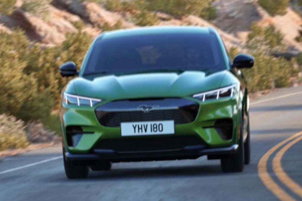 Vedere frontală a unui Ford Mustang Mach-E verde, condus pe drum de munte.