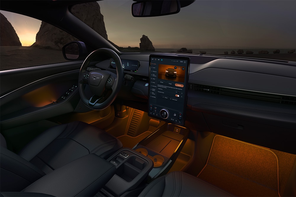 Interiorul modelului Ford Mustang Mach-E pe timp de noapte, care prezintă ecranul tactil SYNC 4 de 15,5" și iluminarea ambientală cu LED-uri setată pe culoarea portocaliu