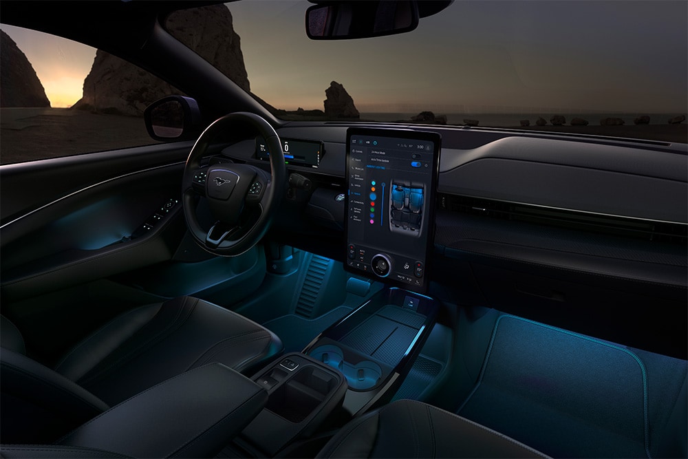 Interiorul modelului Ford Mustang Mach-E pe timp de noapte, care prezintă ecranul tactil SYNC 4 de 15,5" și iluminarea ambientală cu LED-uri setată pe culoarea albastru.