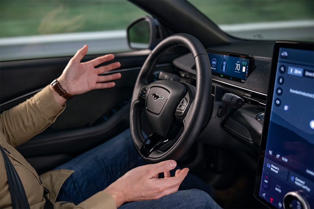 O pereche de mâini trecând ușor pe deasupra volanului modelului Mustang Mach-E, demonstrând tehnologia de condus autonom BlueCruise