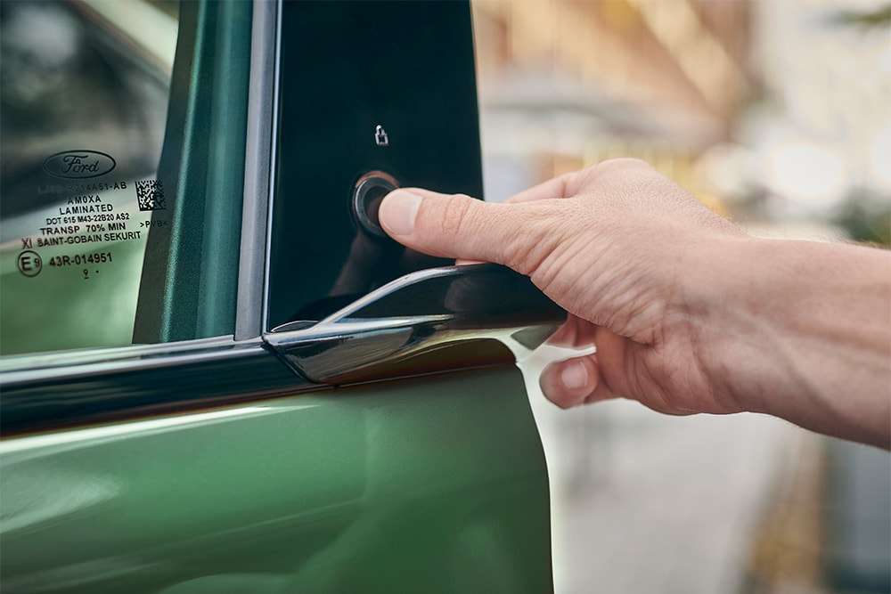 Un prim-plan cu o mână care operează sistemul E-Latch prin apăsarea unui buton pe ușa unui vehicul Ford Mustang Mach-E verde.
