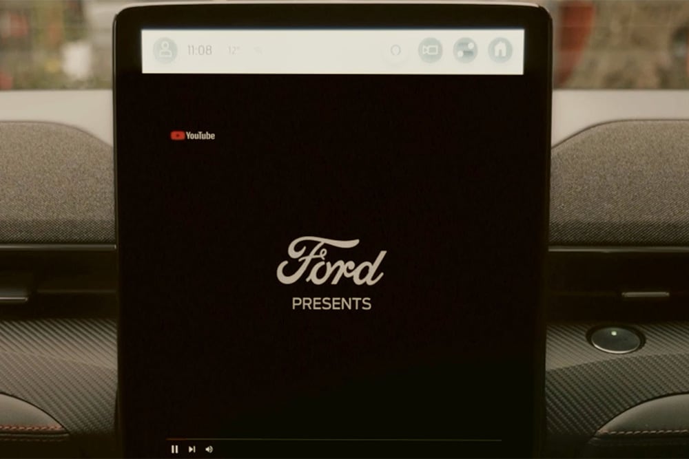 Un prim-plan cu ecranul tactil SYNC 4 de 15,5" cu un grafic pe care scrie „Ford prezintă”, demonstrând transmisia video în mașină