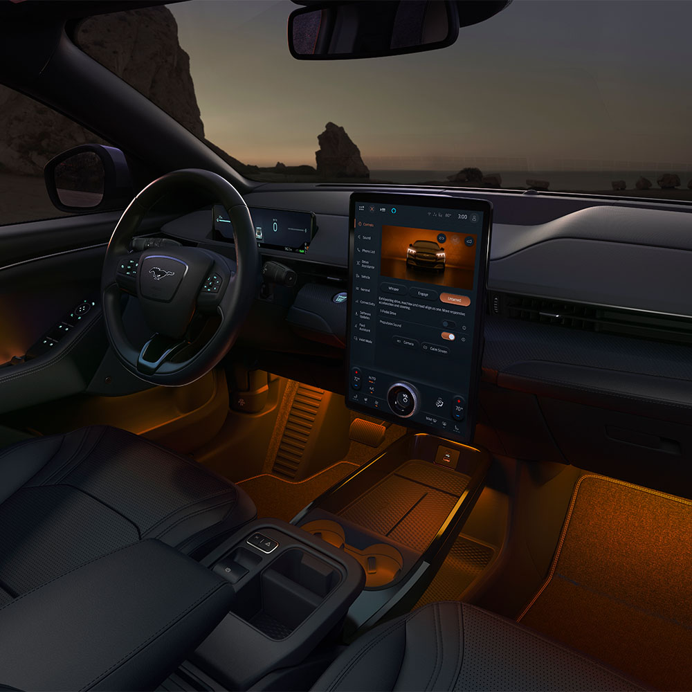 Interiorul modelului Ford Mustang Mach-E pe timp de noapte, care prezintă ecranul tactil SYNC 4 de 15,5" și iluminarea ambientală cu LED-uri setată pe culoarea portocaliu