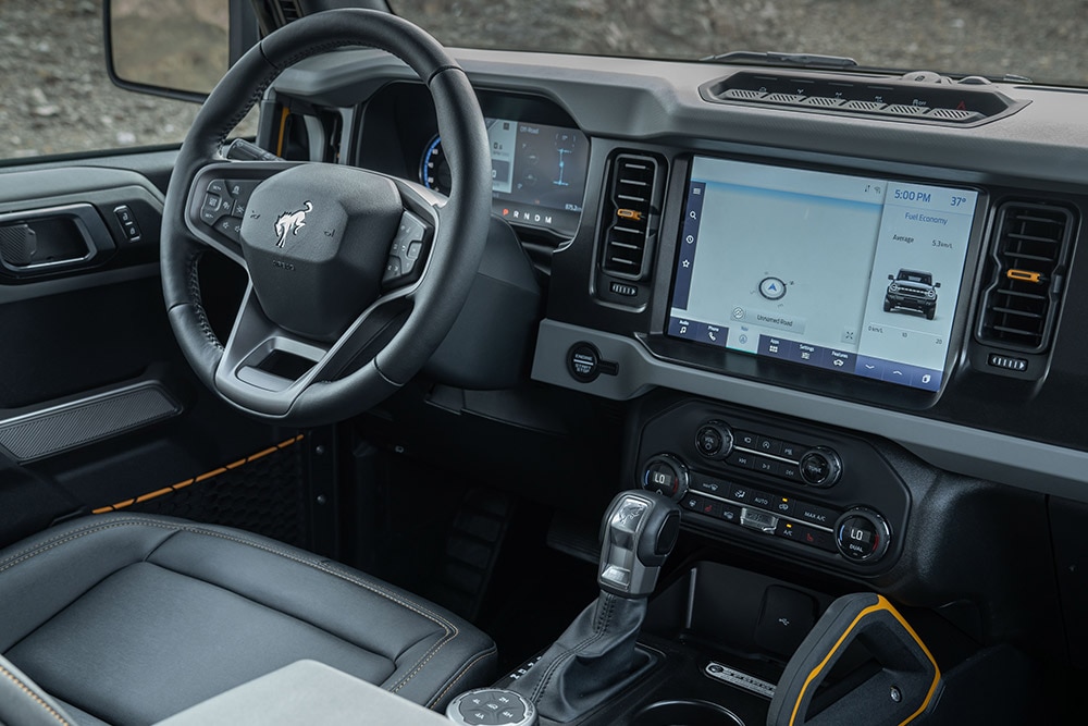 Vedere din interiorul modelului Ford Bronco, incluzând volanul îmbrăcat în piele și touchpad-ul conectat.