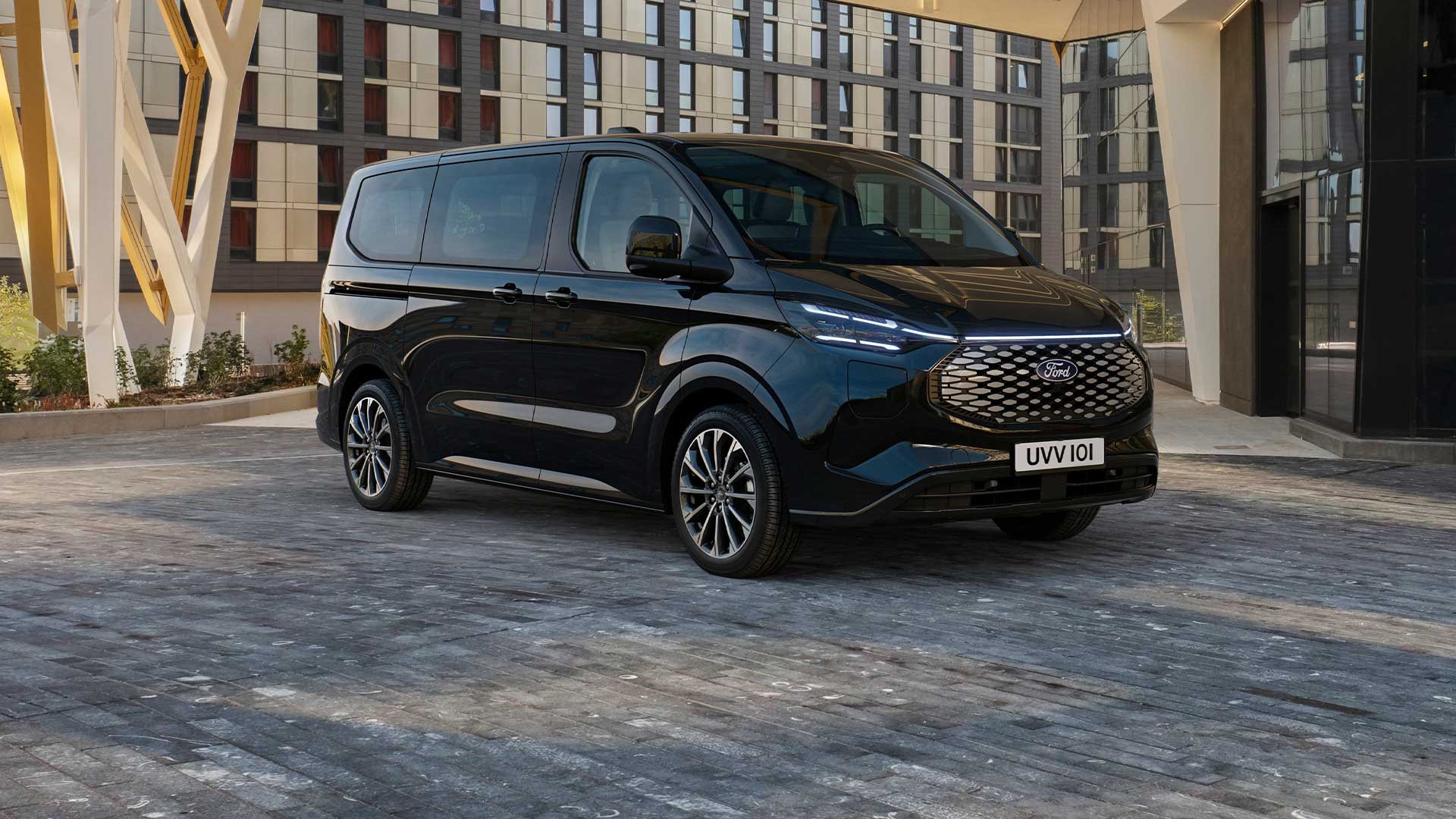 Un Ford E-Tourneo Custom negru este parcat în fața unei clădiri moderne.