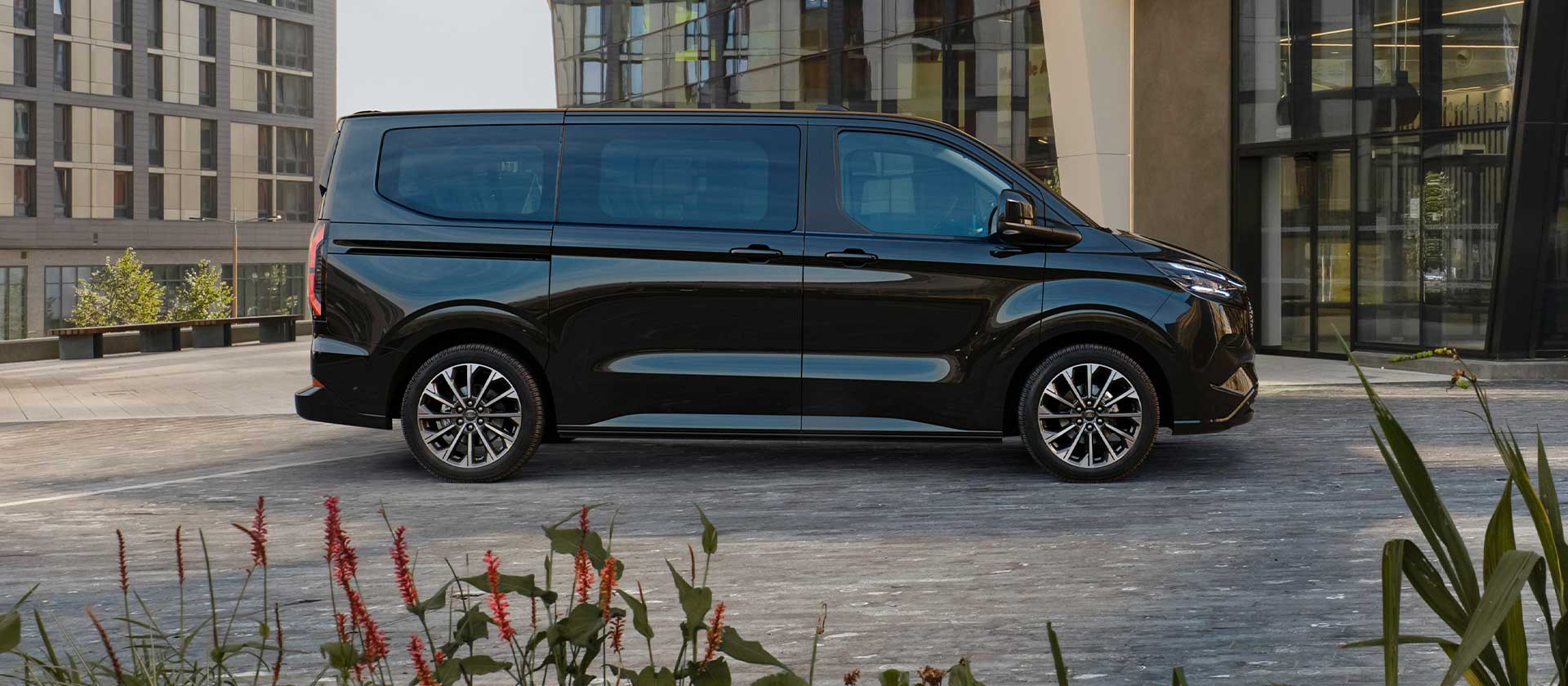 Un Ford E-Tourneo Custom negru este parcat în fața unei clădiri moderne.