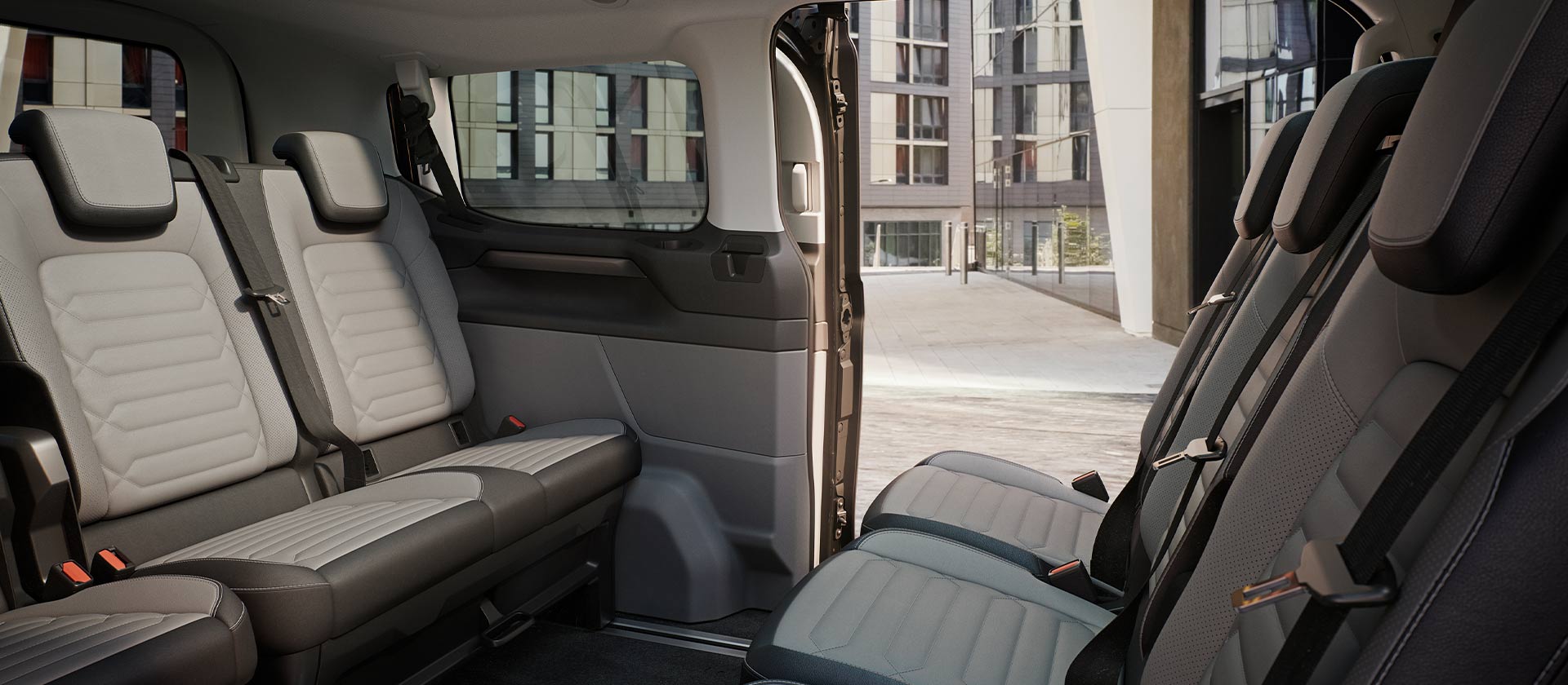 Vedere interioară a Ford Tourneo Custom, cu mai multe rânduri de scaune gri pentru pasageri și plafon panoramic.