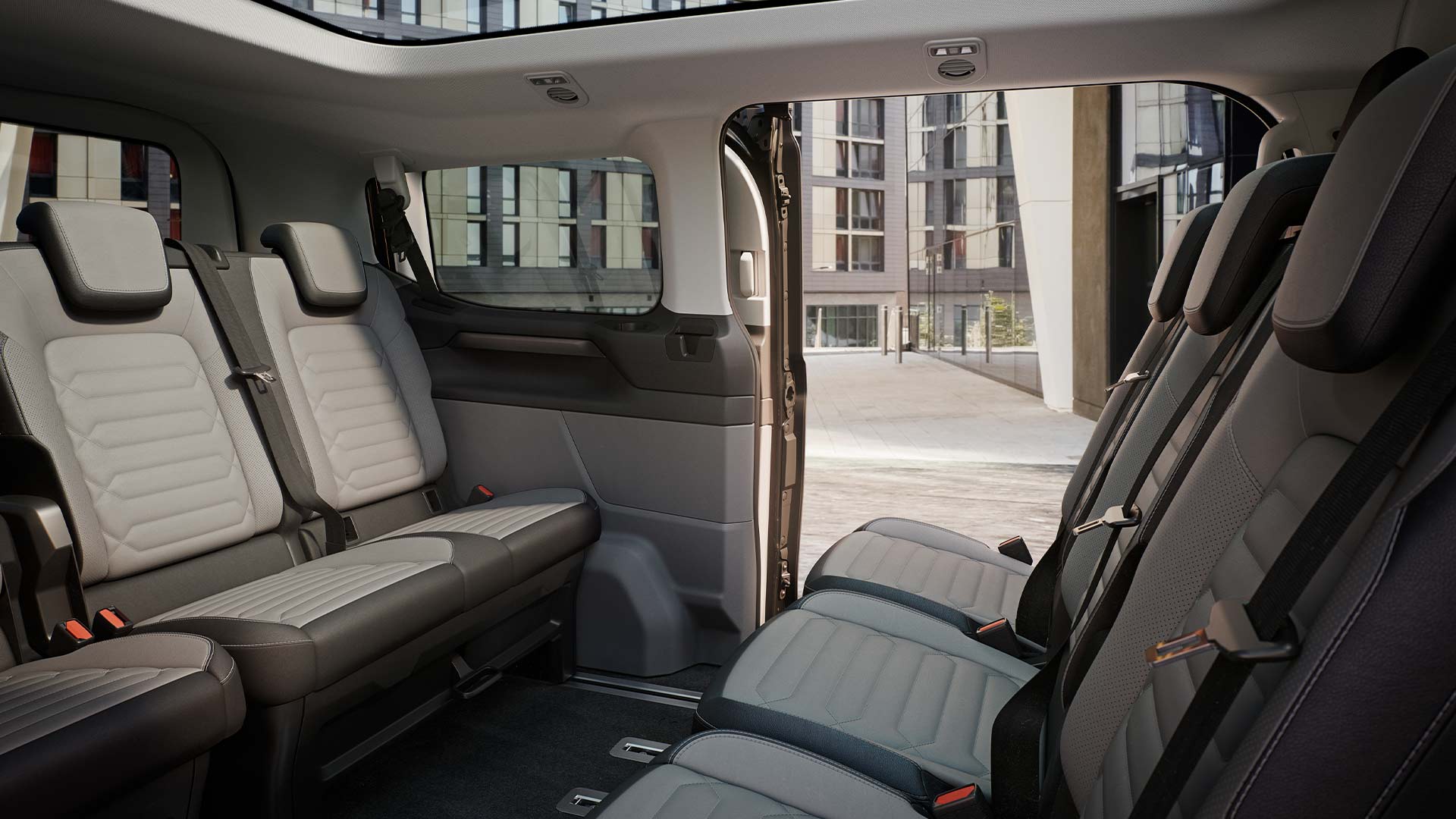 Vedere interioară a Ford Tourneo Custom, cu mai multe rânduri de scaune gri pentru pasageri și plafon panoramic.