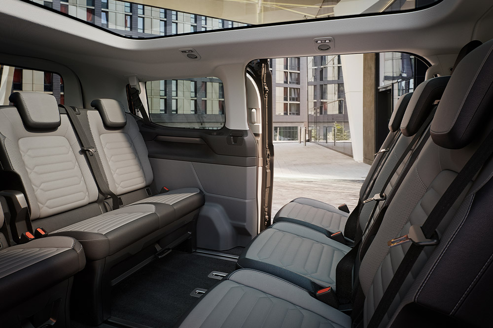 Vedere interioară a Ford Tourneo Custom, cu mai multe rânduri de scaune gri pentru pasageri și plafon panoramic.