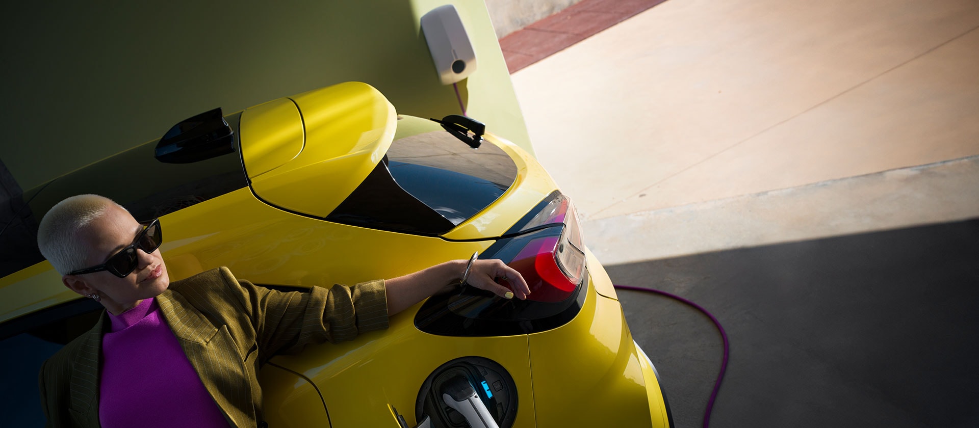 Prim-plan cu partea din spate a Ford Puma Gen-E® electric, galben, conectat la o priză de încărcare de perete pentru acasă.