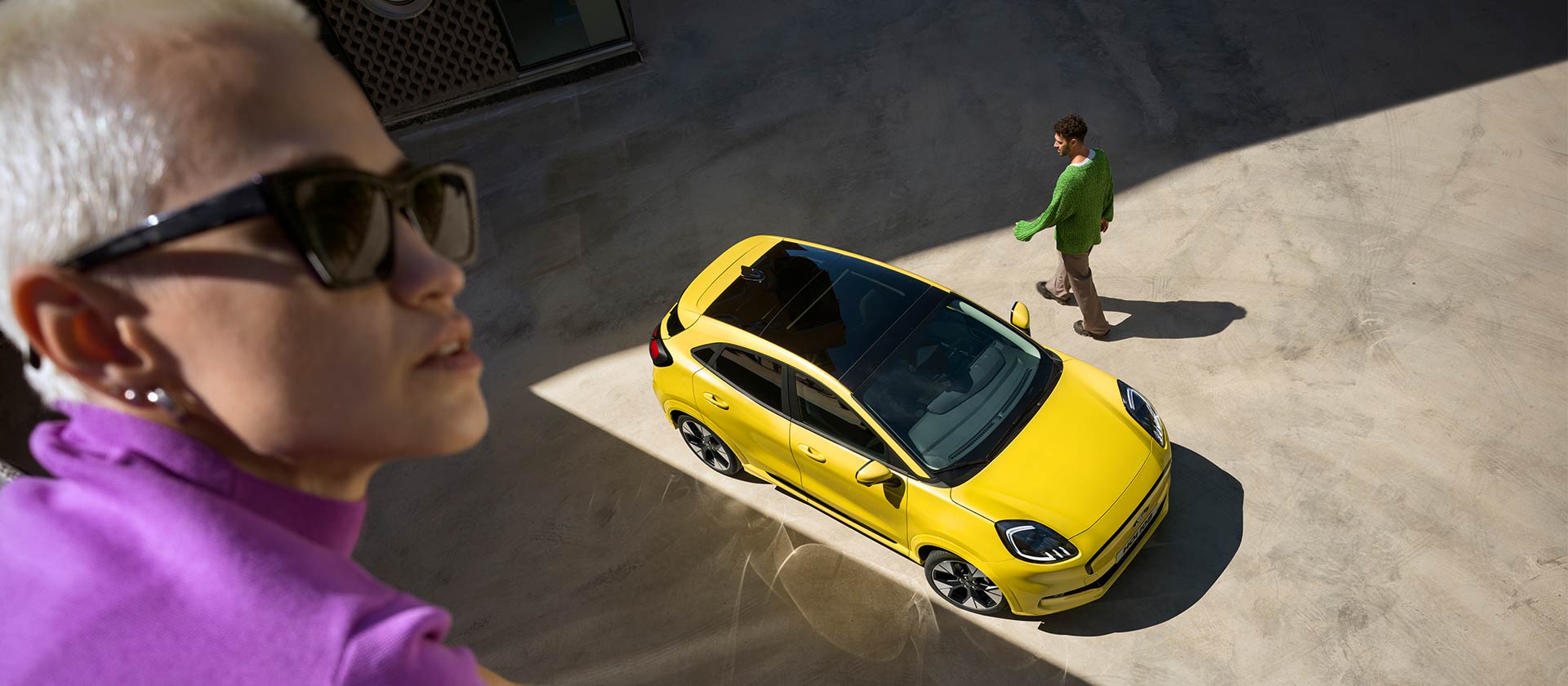 Vedere panoramică a unui vehicul Ford Puma Gen-E® electric, de culoare galben. Persoană în violet aflată în prim plan.