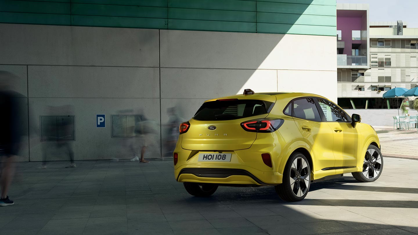 Vedere cu unghiul din spate al unui vehicul Ford Puma Gen-E® electric, de culoare galben, parcat sub un pod.