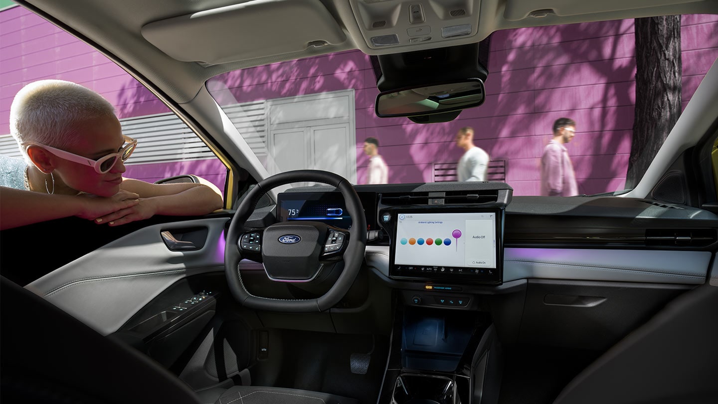 Persoană care privește interiorul noului model Ford Puma Gen-E®, prezentând ecranul mare tactil și iluminarea ambientală.