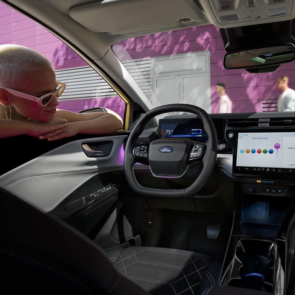 Interior cu modelul Ford Puma Gen-E® electric și cu o persoană care privește prin geam ecranul mare de infotainment.