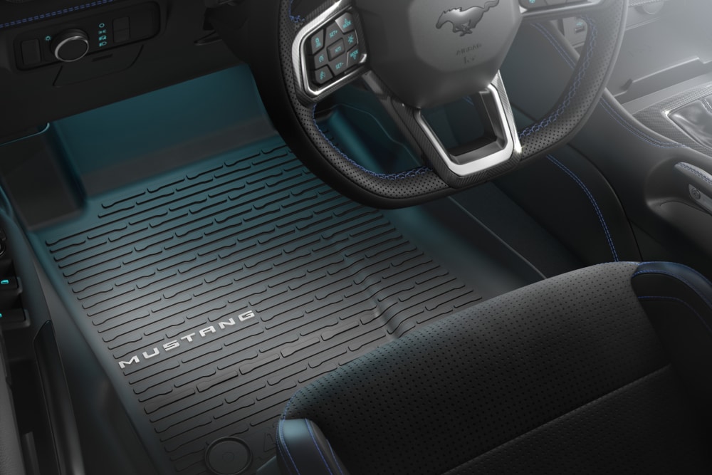 Vedere din interiorul unui Ford Mustang care prezintă volanul și un covoraș pentru toate tipurile de vreme, cu inscripția „MUSTANG”. 
