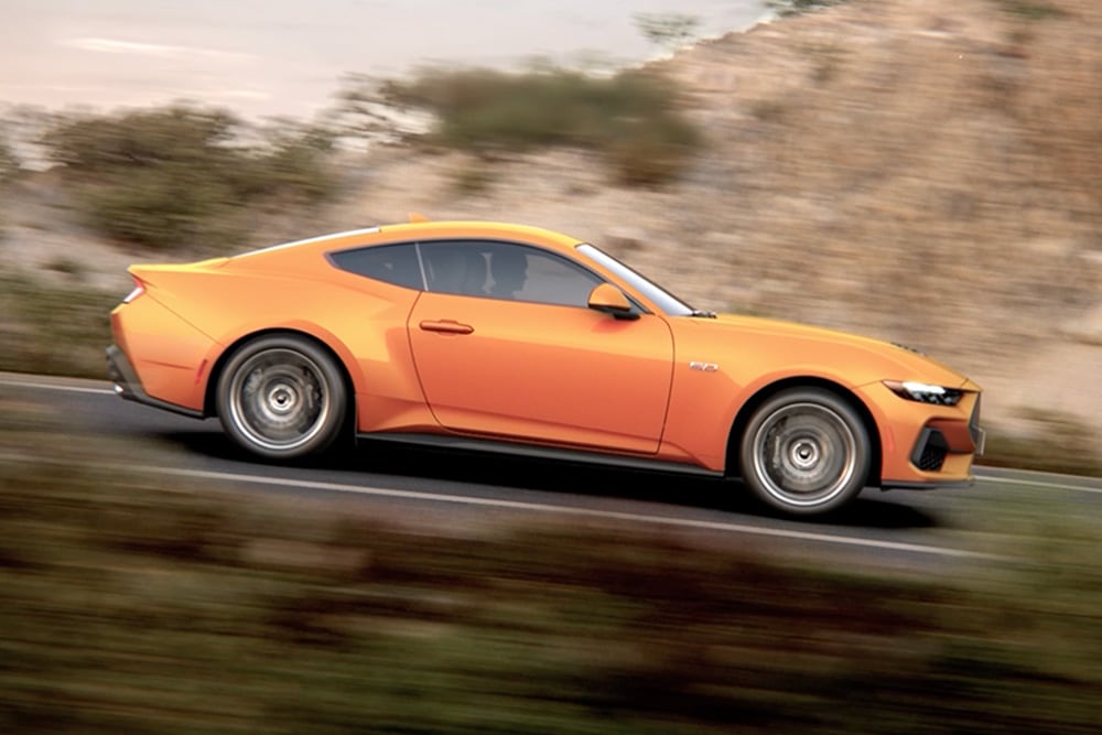 Vedere laterală a Ford Mustang GT Fastback în culoarea Orange Fury, rulând pe un drum
