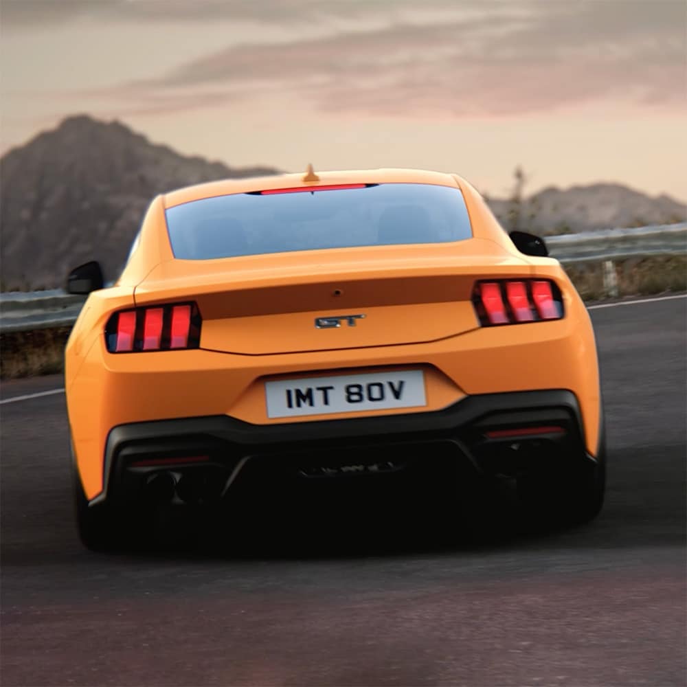 Spatele unui Ford Mustang GT Fastback în culoarea Orange Fury, rulând într-o curbă strânsă pe un drum de țară