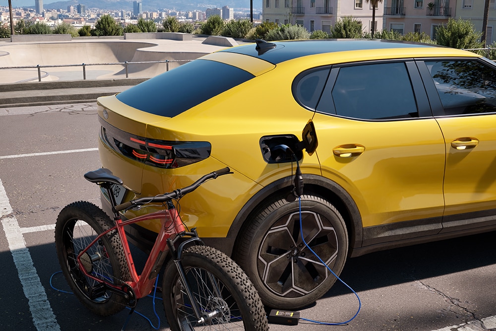 Un Ford Capri® galben parcat, ce încarcă o bicicleta electrică roșie într-un peisaj urban.