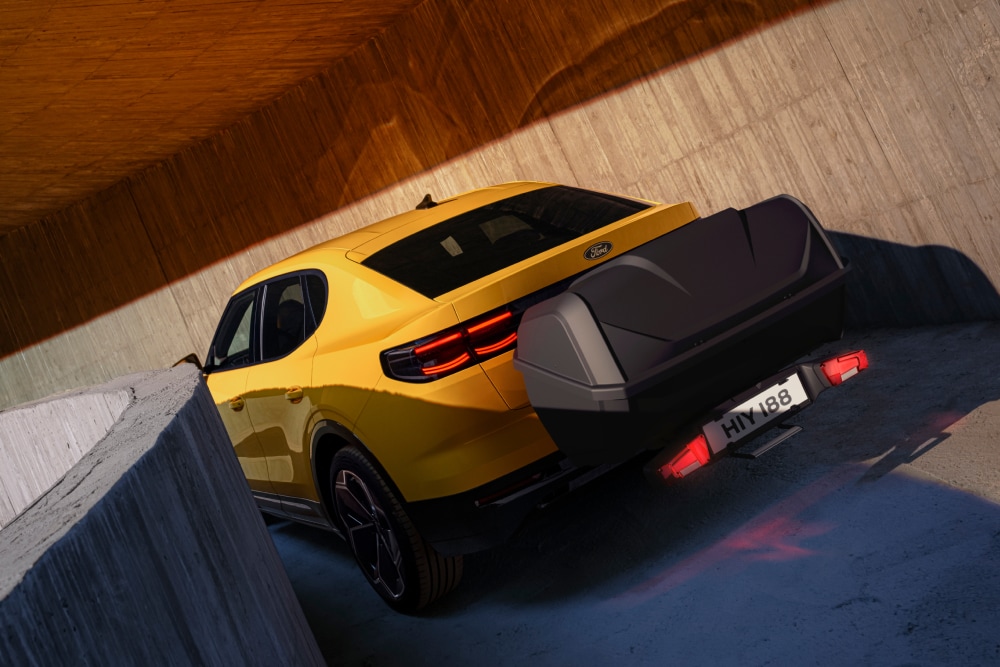 Ford Capri galben parcat pe o structură modernă din beton, vedere din spate care prezintă un portbagaj atașat la spate cu un suport specific.