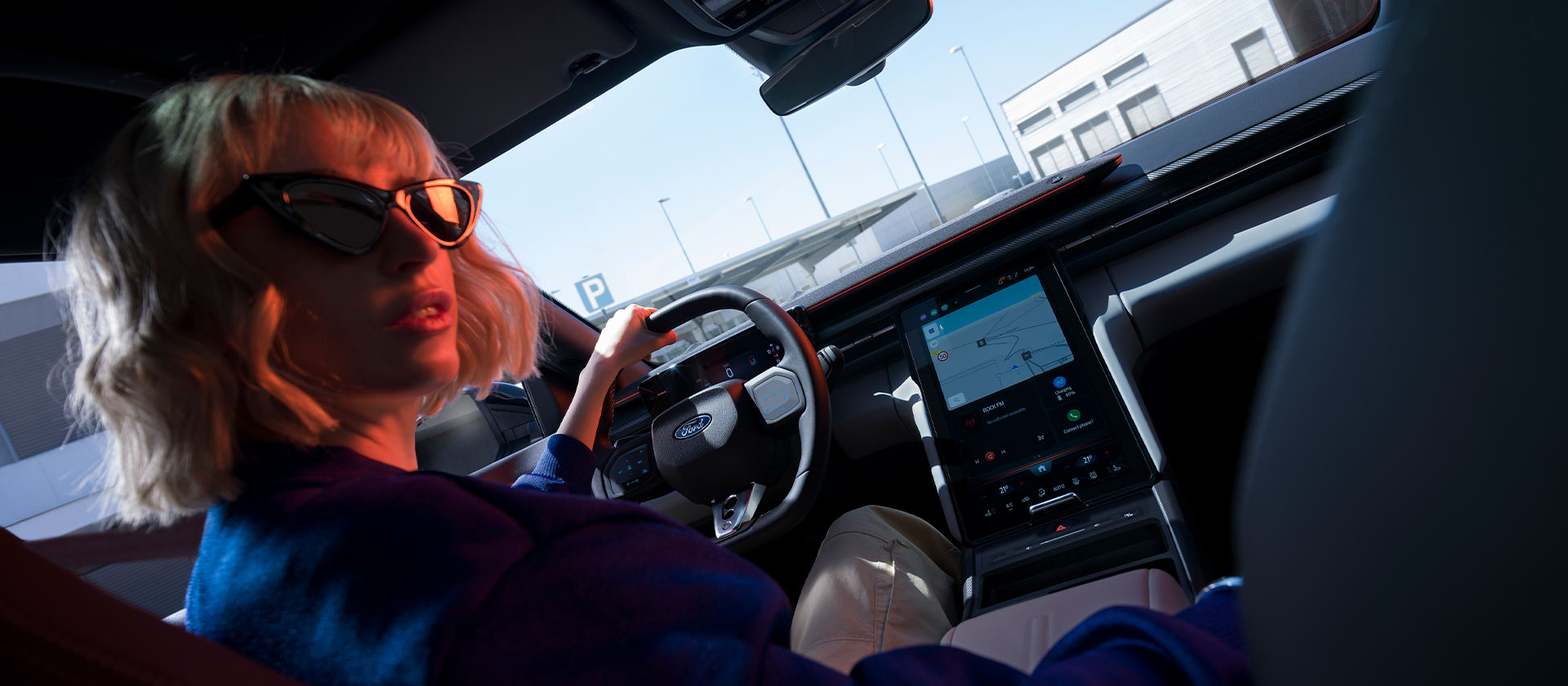 O femeie stă pe scaunul șoferului unui model Ford Capri® parcat, în imagine fiind vizibile volanul și ecranul mare SYNC®.