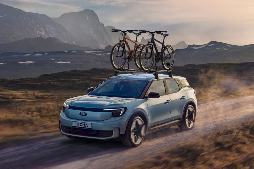 Ford Explorer albastru deschis, condus pe drum neasfaltat, dotat cu bare transversale și două biciclete montate pe suporți pe plafon.