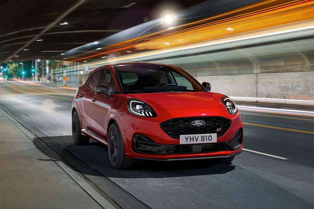 O mașină Ford Puma ST SUV sport care circulă pe un drum urban puternic luminat pe timp de noapte.