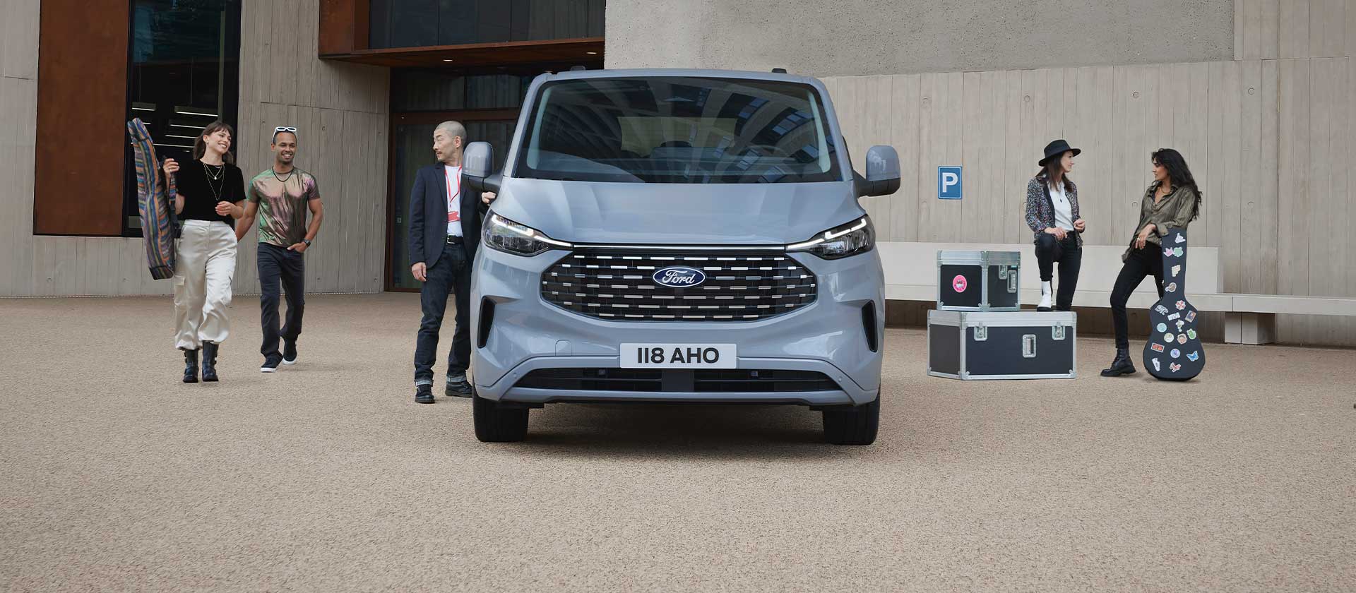 Un grup  de muzicieni care stau lângă un Tourneo Custom Van de culoare gri argintie