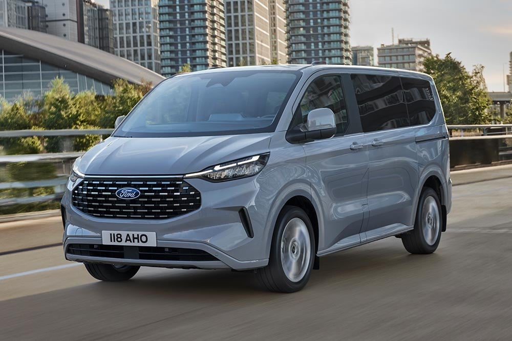 Un Ford Tourneo Custom argintiu se deplasează pe un drum urban.