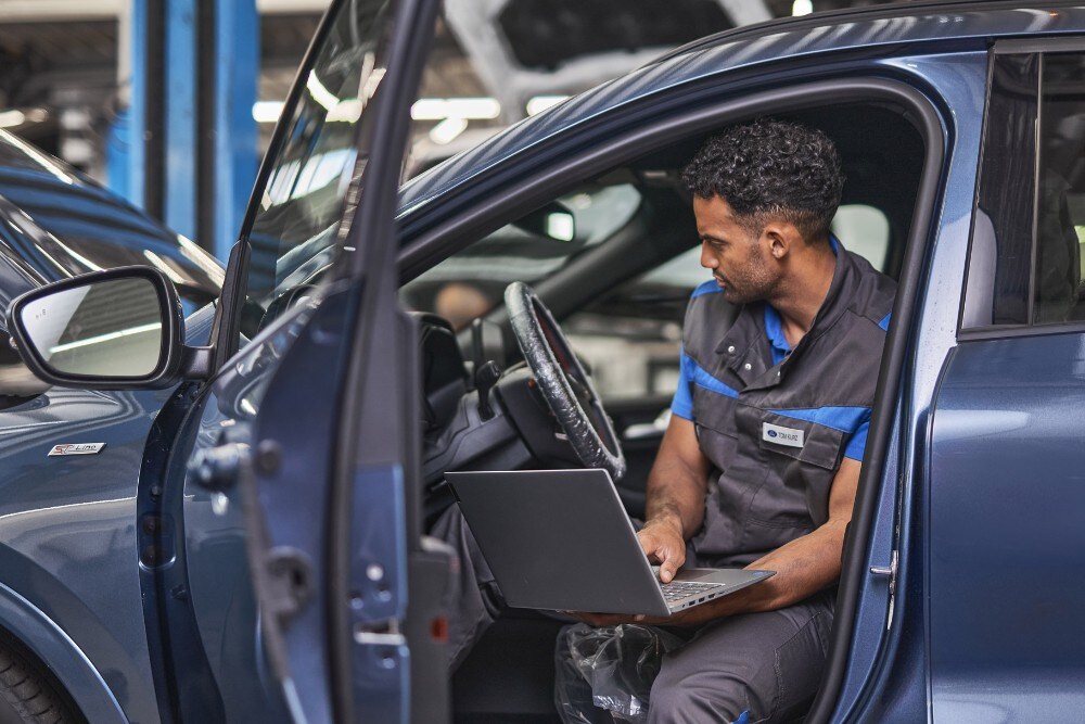 Tehnician Ford folosește un laptop în timpul întreținerii unui vehicul cu portiera șoferului deschisă. 