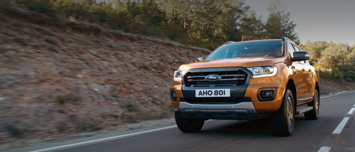 Orange Ford Ranger Wildtrak driving through a forest, front three quarter view