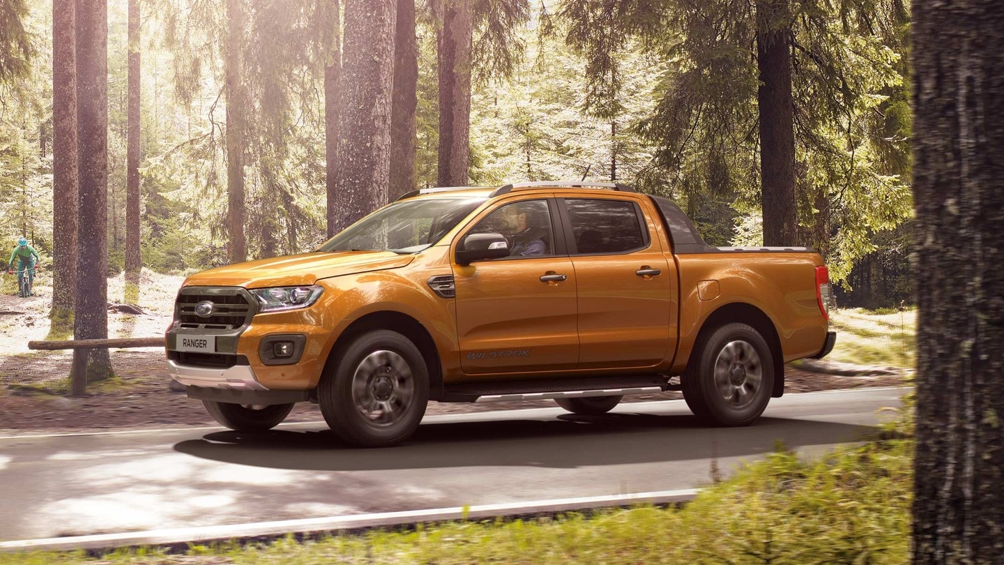 Soarele strălucește pe Ford Ranger Wildtrak portocaliu parcat pe un drum forestier, vedere laterală