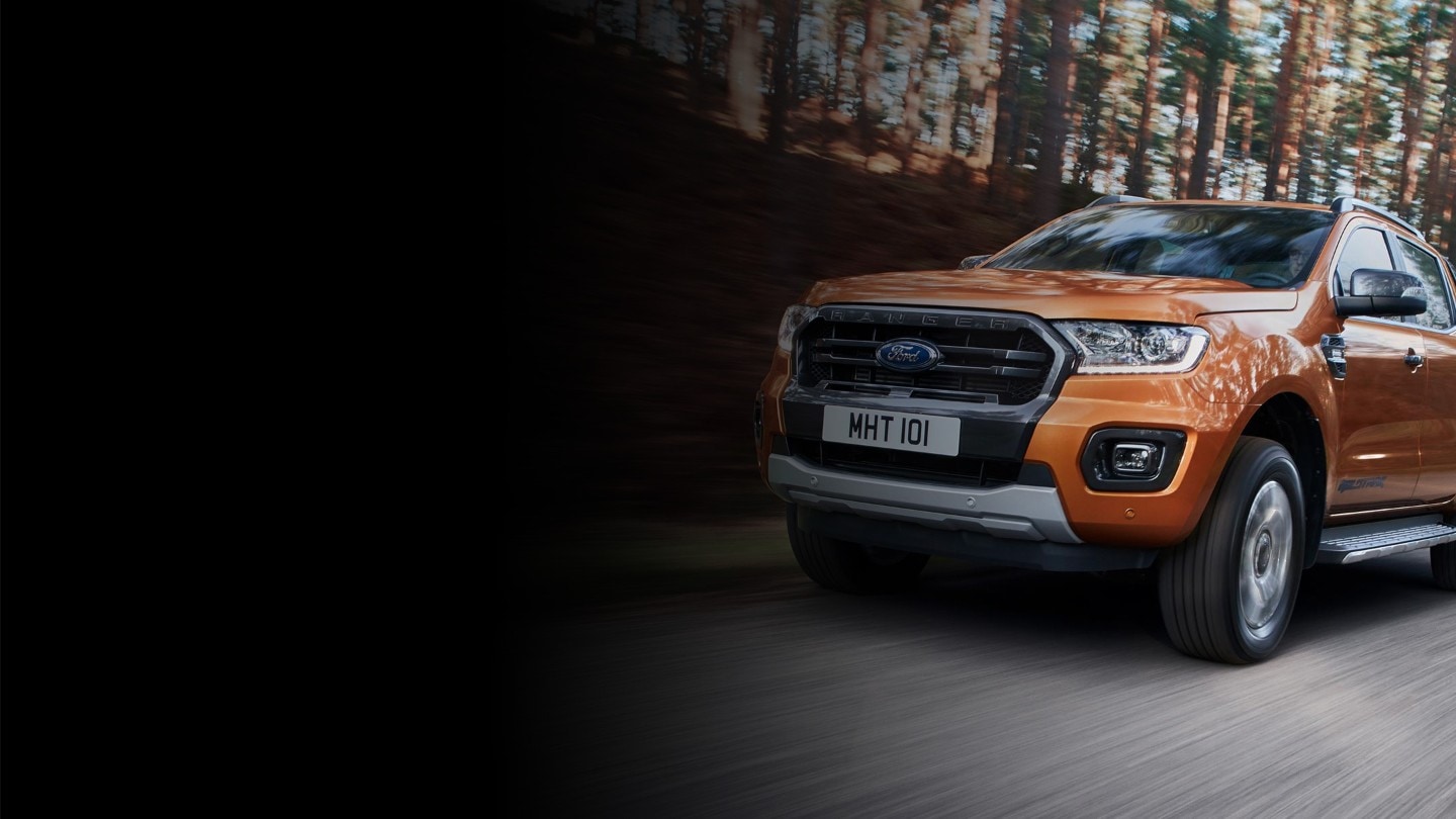 Orange Ford Ranger Wildtrak driving through forest, front seven eighths view