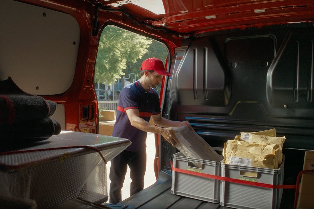 Curier încărcând pachete într-un Ford E-Transit Customde culoare roșie.