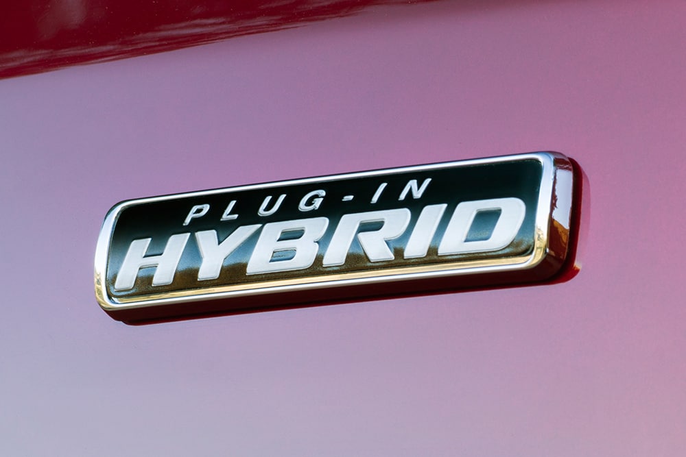 Prim-plan cu emblema Plug-in Hybrid de pe un Ford Transit Custom roșu.