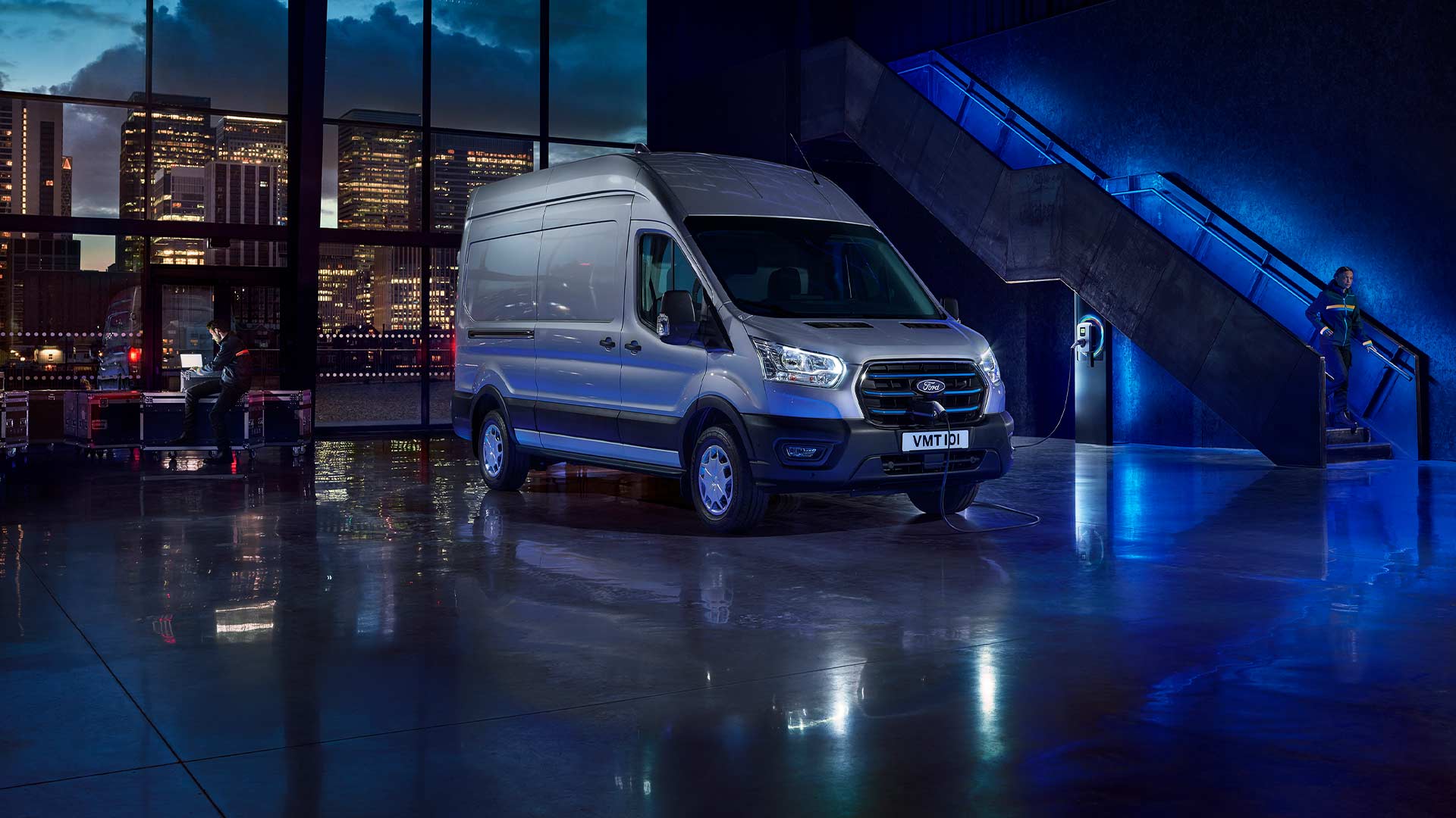  Ford E-Transit Furgon  culoare Moondust Silver parcat în interior cu priveliștea orașului vizibilă prin ferestrele mari. 