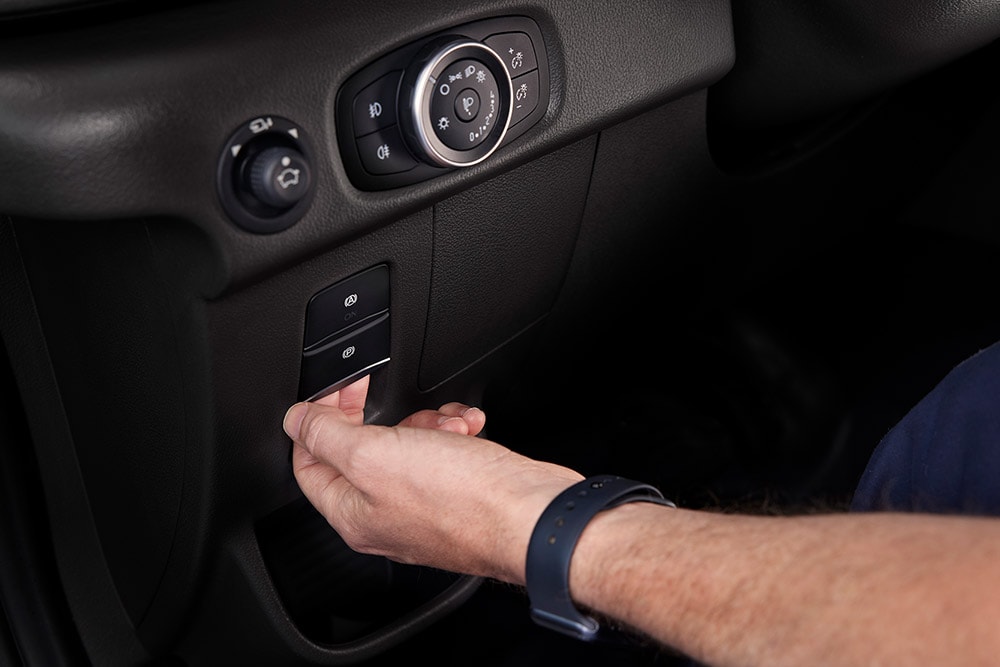 Prim-plan cu o mână care apasă un buton de pe tabloul de bord al unui furgon Ford E-Transit.