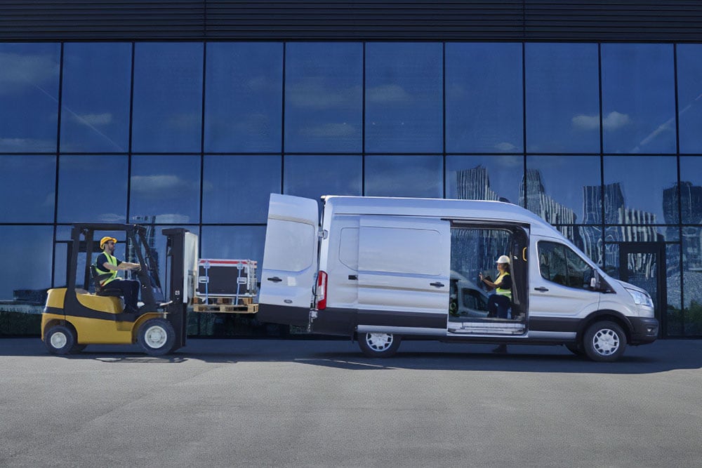 Două persoane care încarcă marfă într-un  Ford Transit Furgon, Moondust Silver , cu un stivuitor.