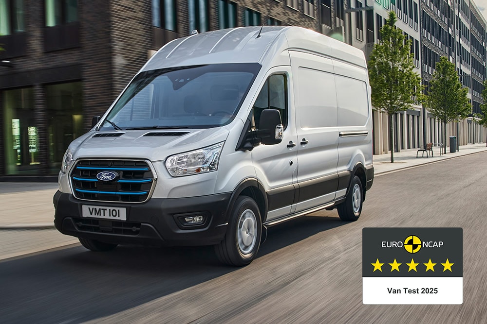 Ford E-Transit Furgon , Moondust Silver,  care se deplasează pe un drum cu o insignă „Gold 2022 Commercial Van Safety”.
