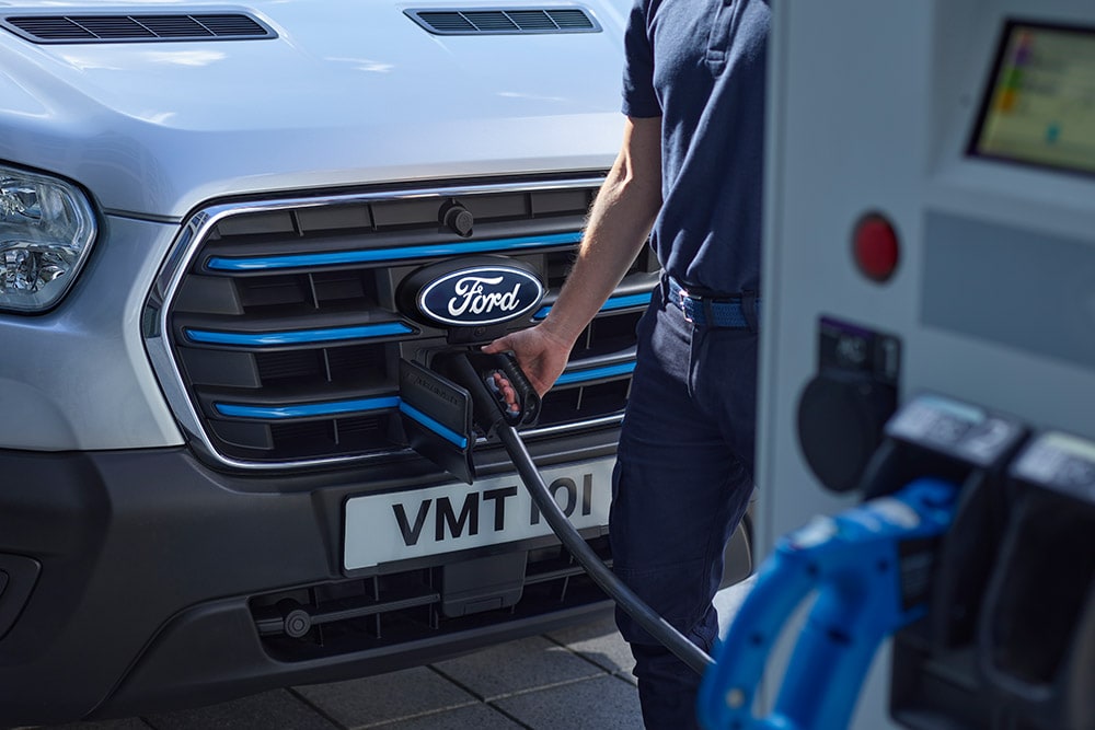 Prim-plan cu o persoană care conectează un cablu de încărcare la o furgonetă electrică Ford E-Transit Moondust Silver