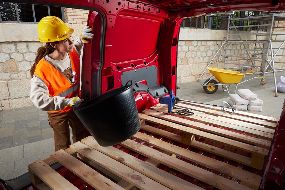 O femeie pune materiale de construcție în spațiul de încărcare al unui Ford Transit Connect, cu ușile laterale și din spate deschise.