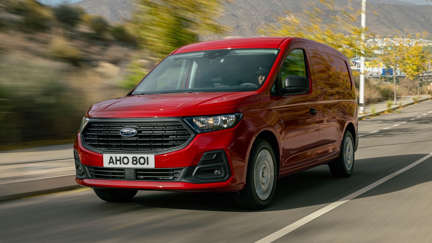Noul Ford Transit Connect în culoarea Maple Red se deplasează pe o șosea prezentând grila frontală și farurile automate.