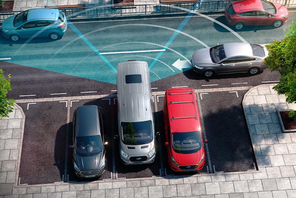 Furgonetă Ford Transit argintie care merge cu spatele, cu linii albastre care indică utilizarea senzorului de parcare cu spatele.