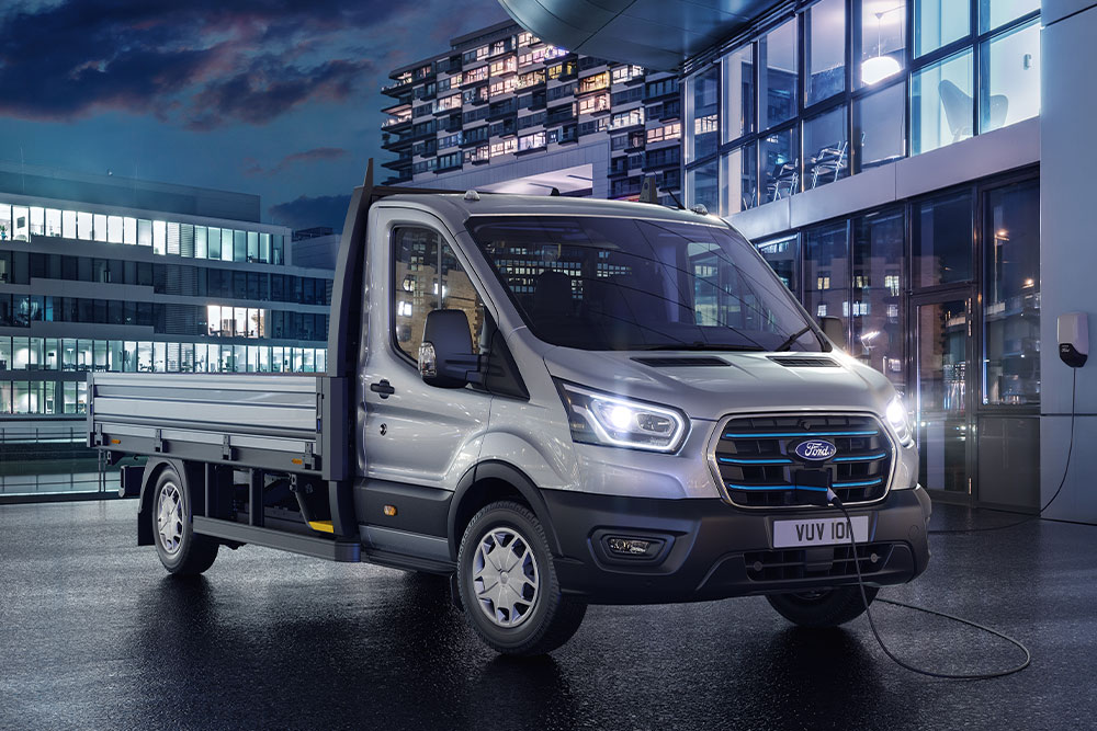 Ford E-Transit Autoșasiu cu Cabină  Simplă  argintiu parcat în fața unei clădiri moderne, noaptea.